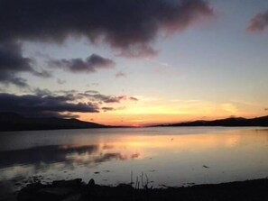 Un lago tranquilo al atardecer con cielo despejado y montañas a lo lejos.
