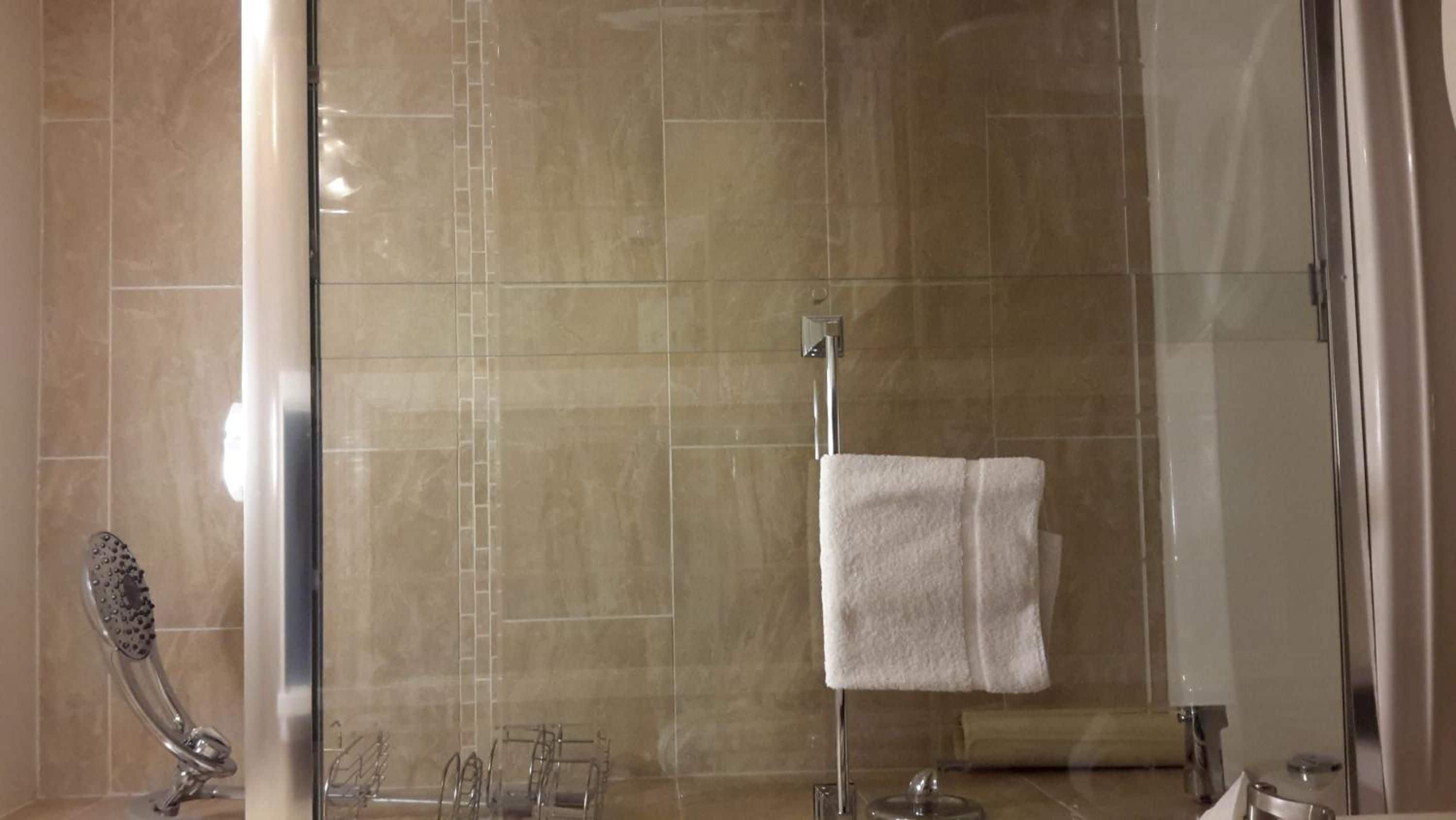 A bathroom with a glass shower enclosure, a towel rack with a white towel, and a showerhead.