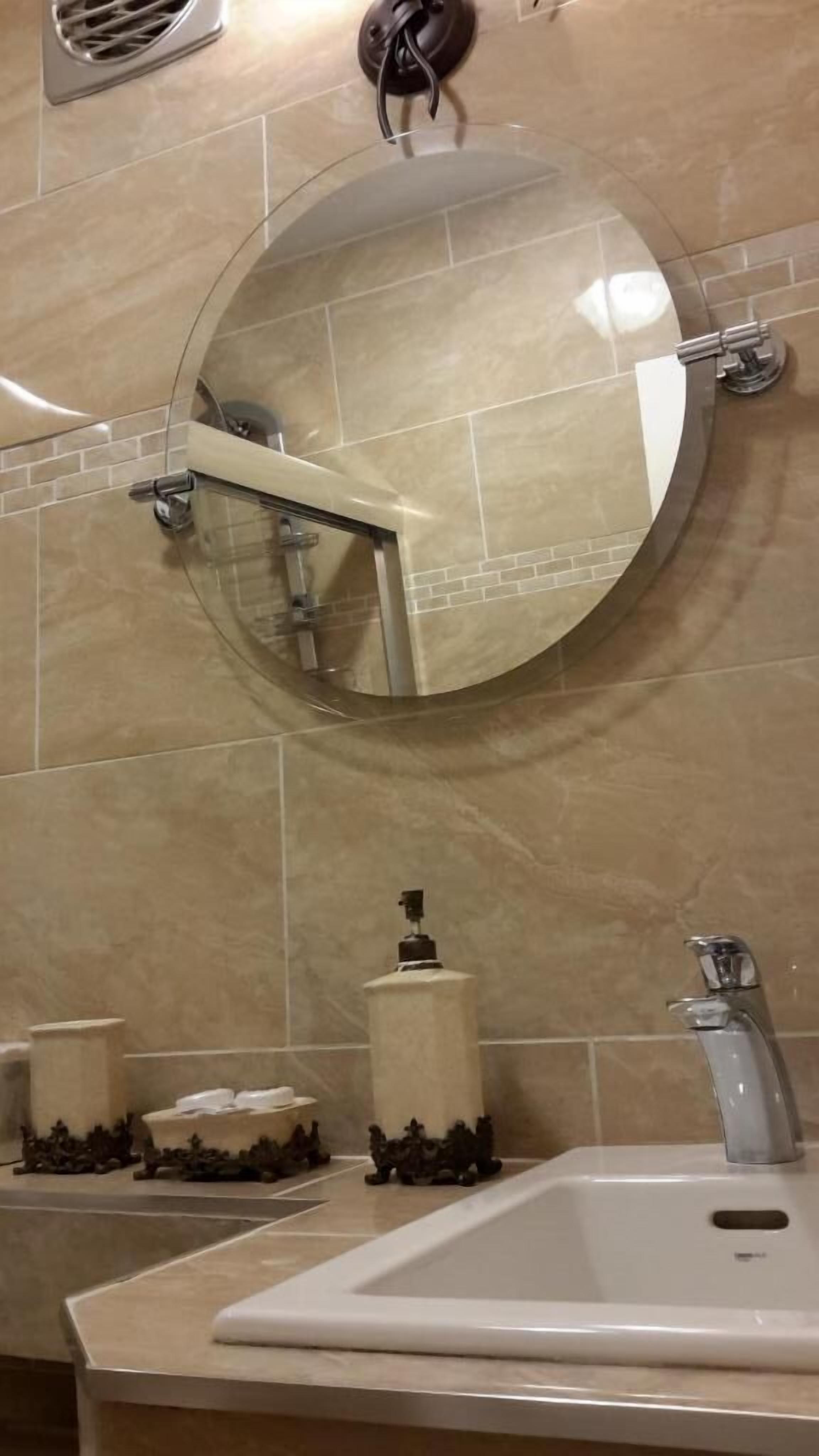 Une salle de bain avec un miroir rond, un lavabo, un distributeur de savon et un porte-serviettes.