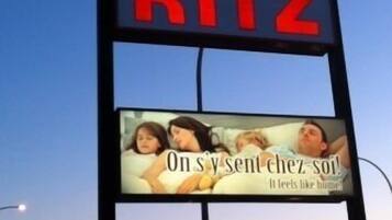 A motel sign with the name 'MOTEL RITZ' and an advertisement below featuring a family.