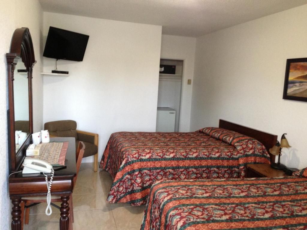 Habitación de hotel con cama, escritorio con teléfono, una silla, televisor montado en la pared y puerta que da a un armario.