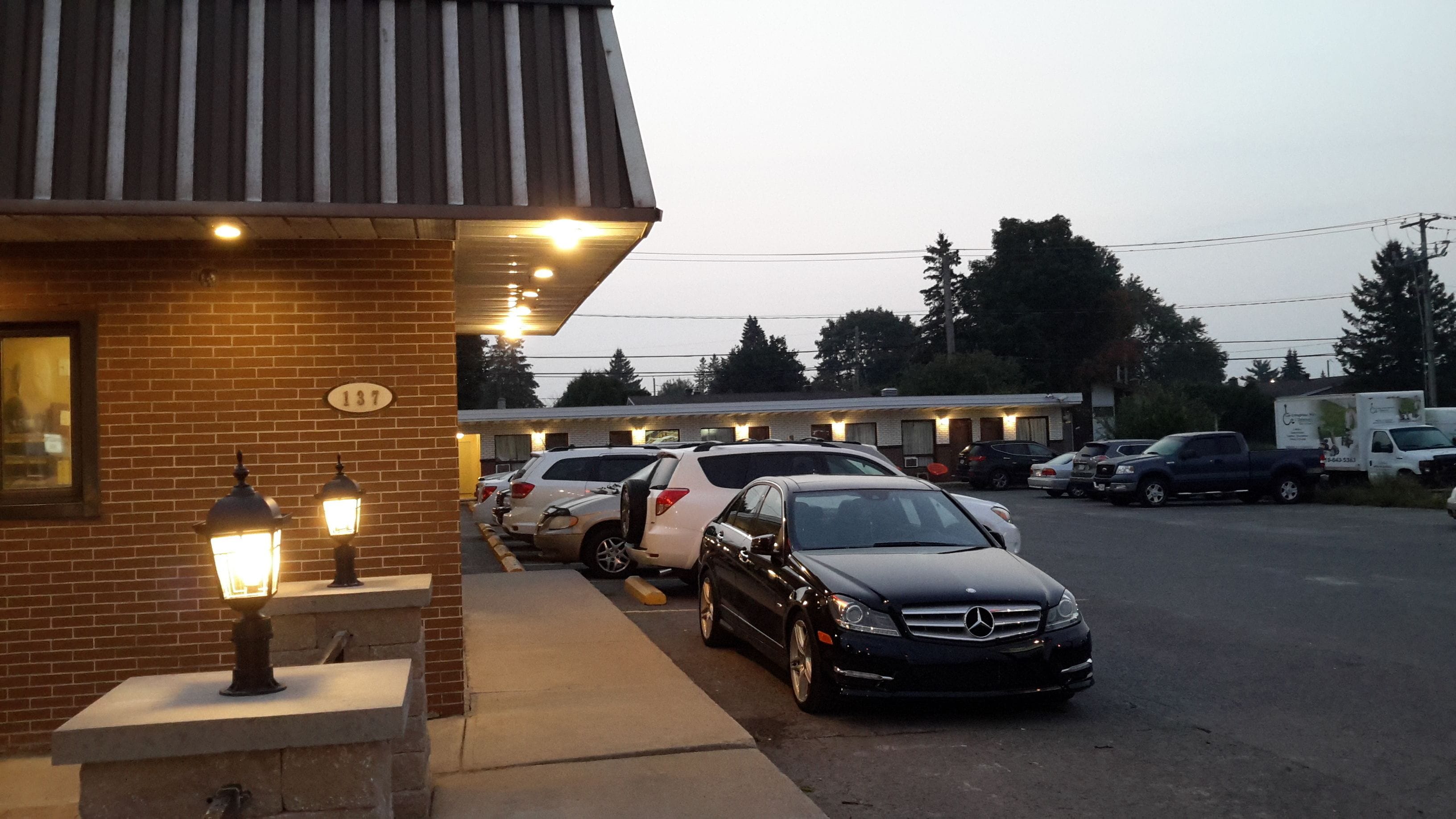 A building with a brick facade, a number '137' sign, and a row of parked cars including a black Mercedes-Benz.