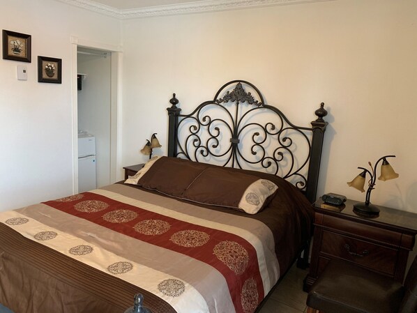 A neatly made bed with a patterned bedspread, a decorative headboard, bedside lamps, and a small wooden nightstand with a radio. - Motel Ritz (Gatineau)