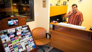 A man in a red shirt at a counter with a telephone, surrounded by various movie posters and a wooden desk. - Motel Ritz (Gatineau)
