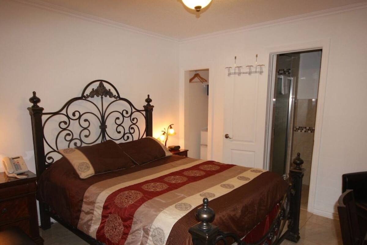 A bedroom with a four-poster bed, a bedside table with a lamp, a chair, and a door with a mirror.