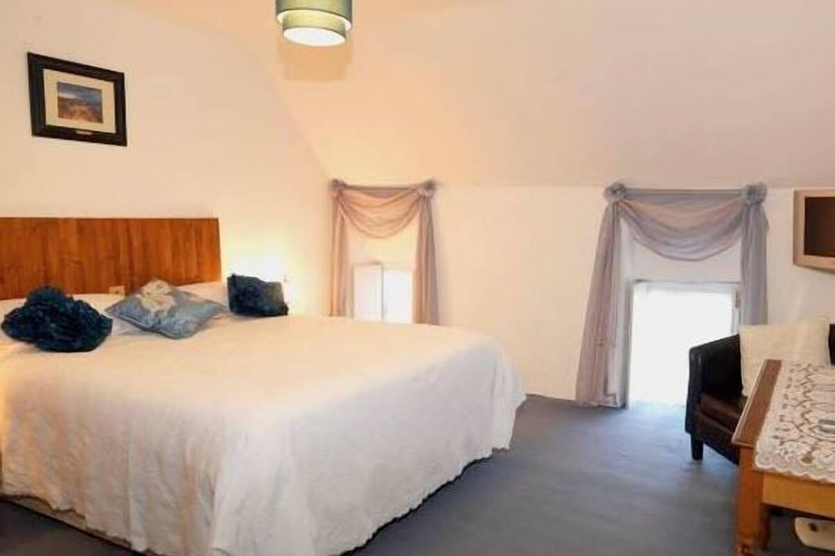 A bedroom with a bed, a wooden headboard, a nightstand, a chair, and a window with curtains.