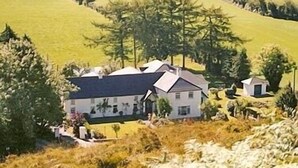 A house with a large front lawn, a smaller outbuilding, and a wooded area in the background. - Salmon Leap Farm B&B (Killarney)