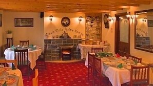 A cozy restaurant with wooden walls and a stone fireplace. Tables are set with white tablecloths and green napkins. - Salmon Leap Farm B&B (Killarney)