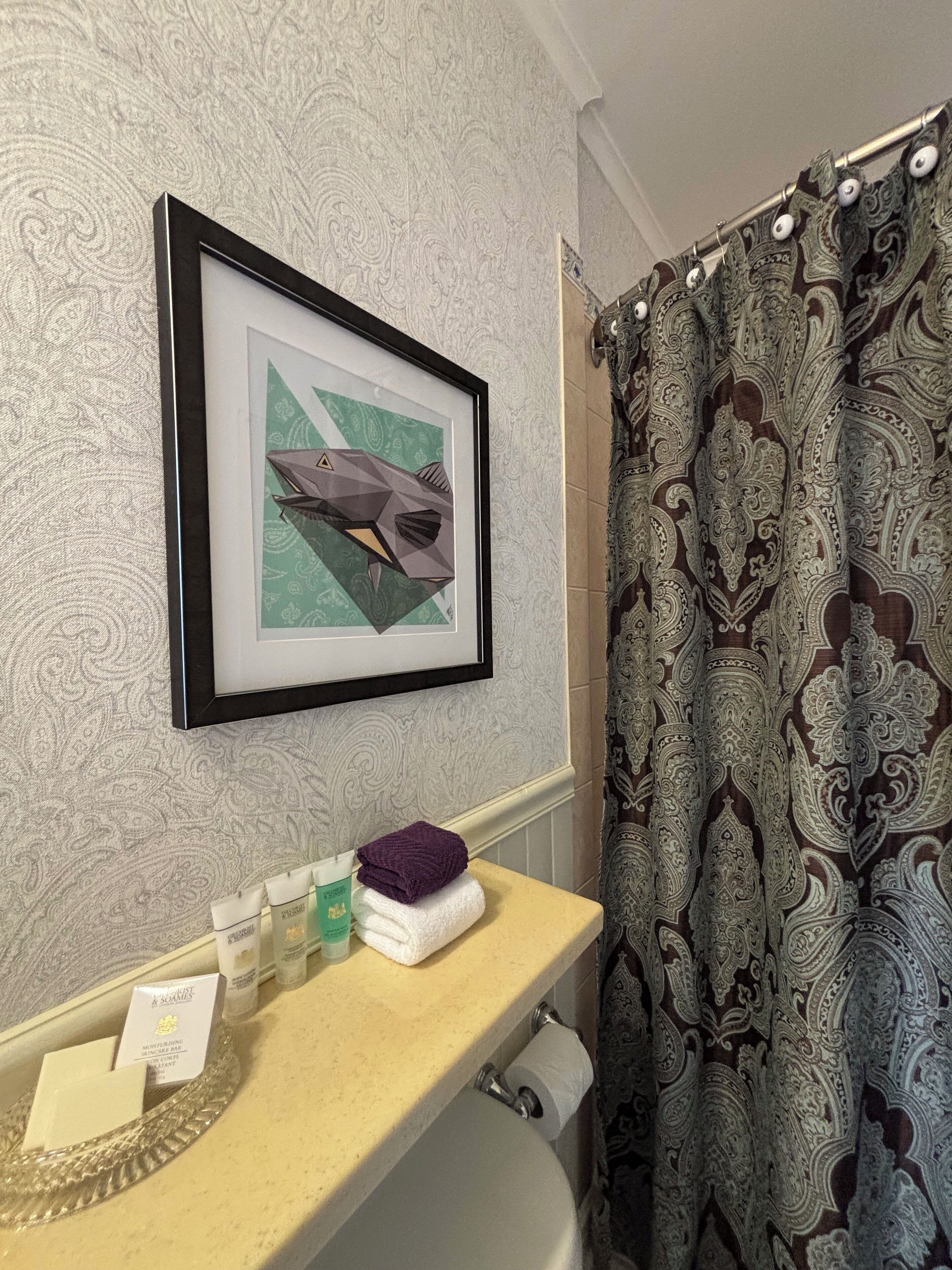 A bathroom with a framed picture of a shark, a towel, toiletries, and a shower curtain.