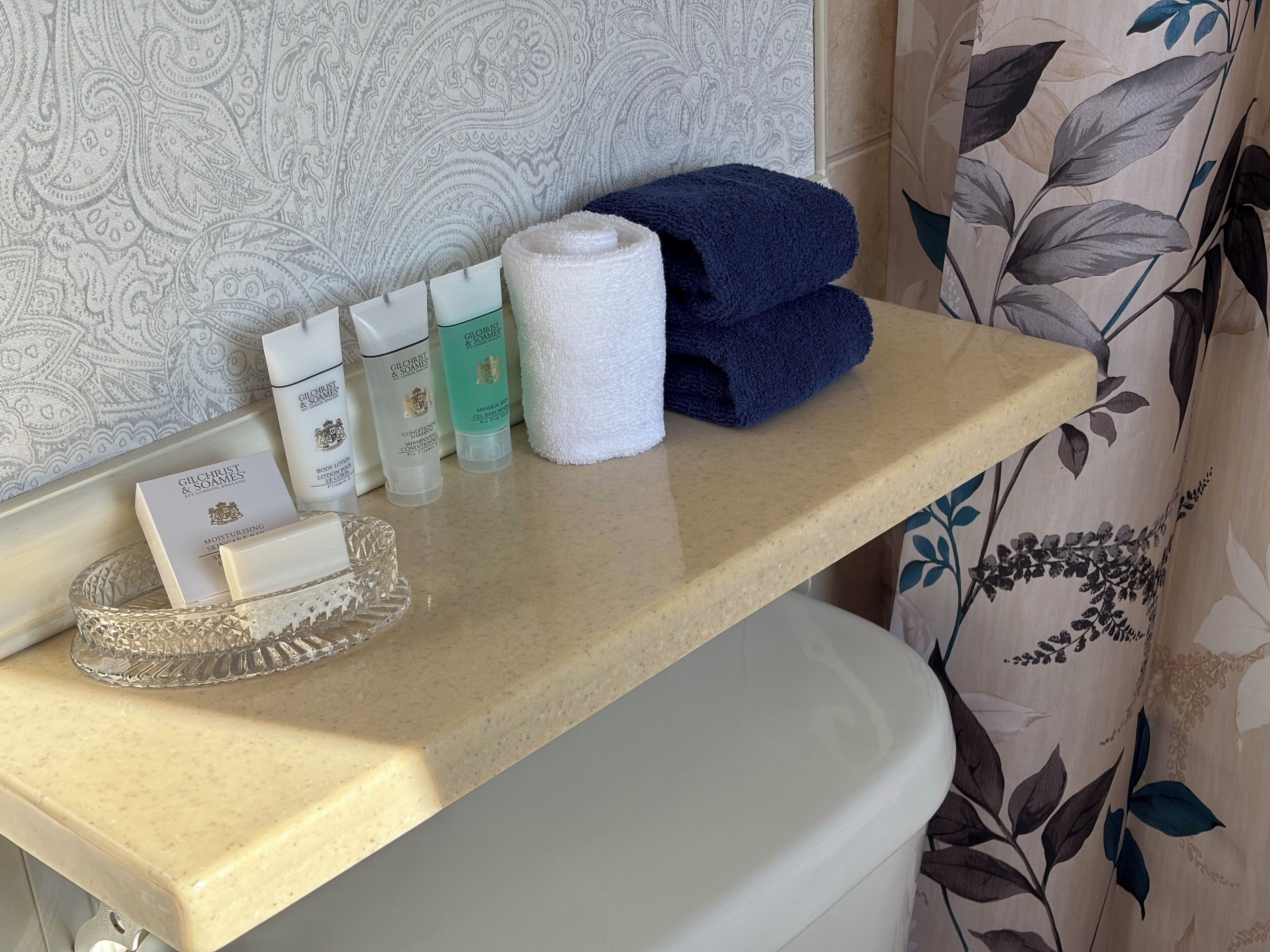 A bathroom vanity with toiletries, a white towel, and a blue towel on a beige countertop.
