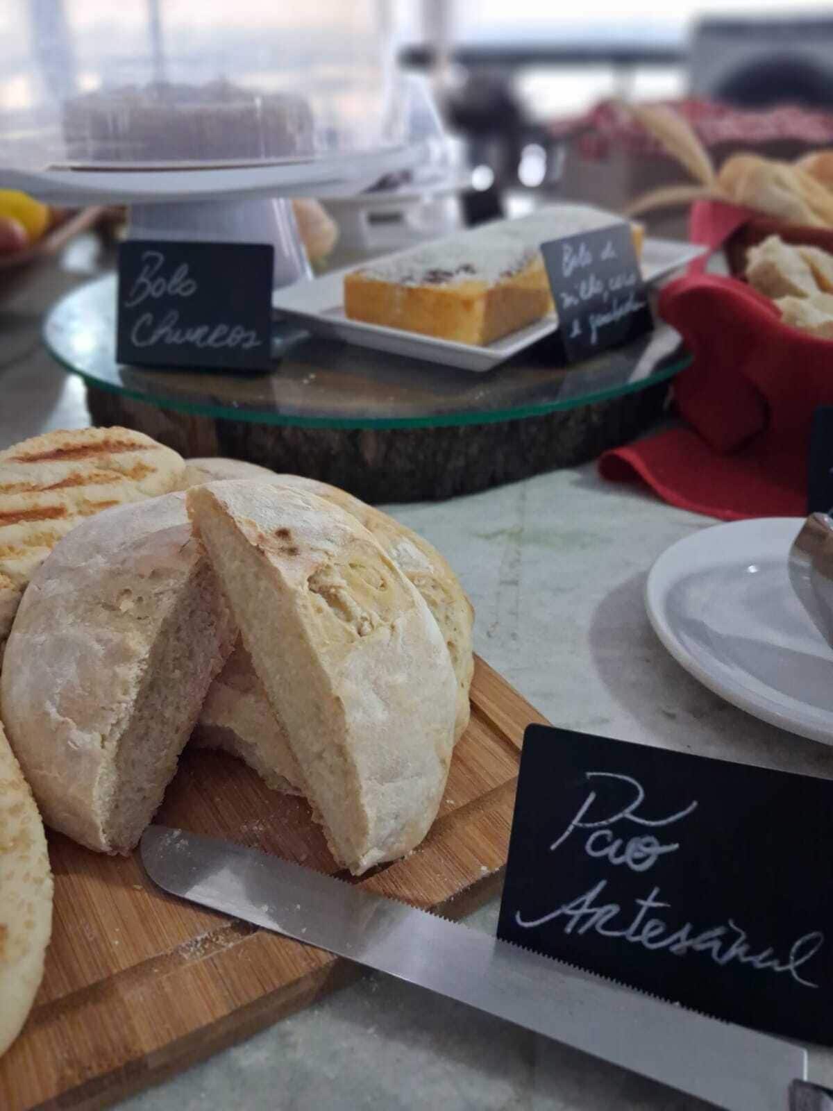 A bakery display with various breads and pastries, including a sign that reads "Pao Artesanal".