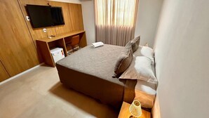 A bedroom with a bed, a TV mounted on the wall, a desk with a chair, and a window with curtains. - Hotel Amazônico (Belém)