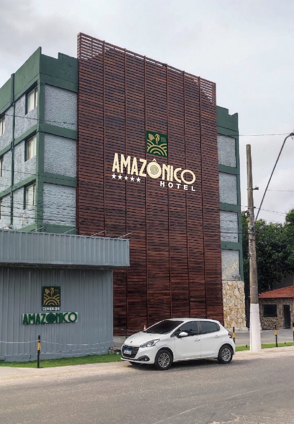 Un edificio moderno con un llamativo letrero que dice 'AMAZONICO HOTEL', que presenta una fachada única con listones verticales y un techo verde.