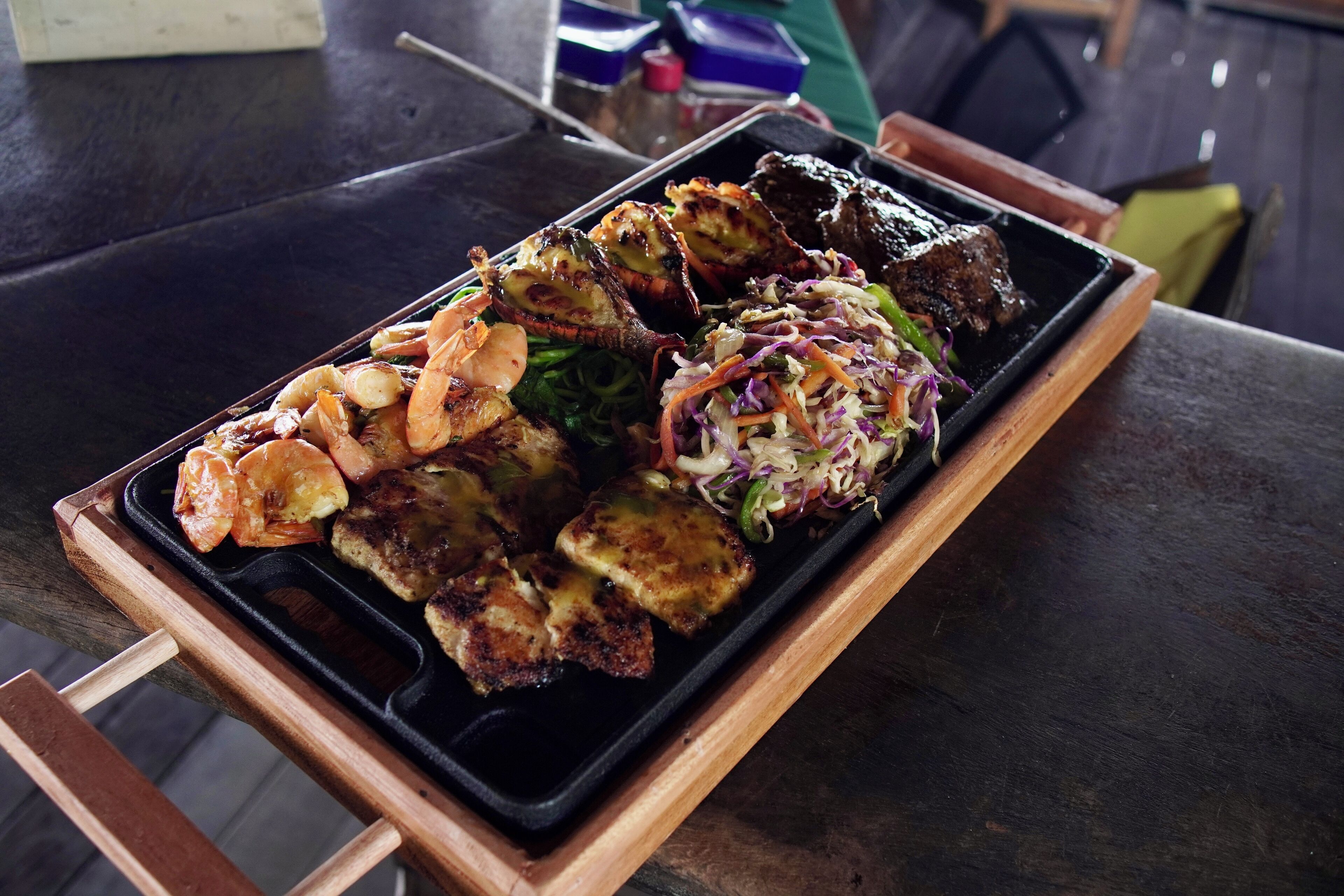 Bandeja de comida con camarones a la parrilla, carne y verduras sobre una mesa de madera.