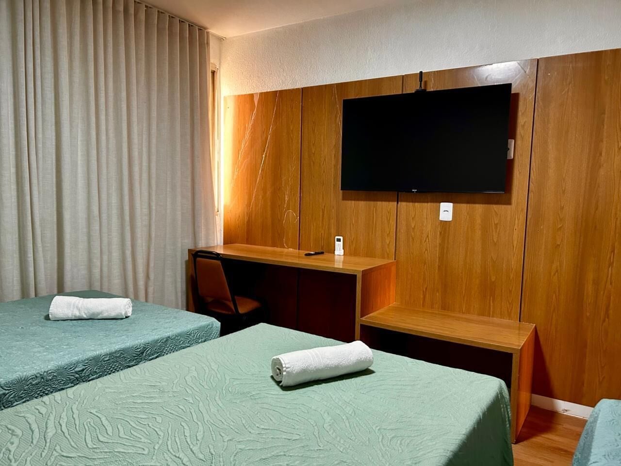 Ein Hotelzimmer mit zwei Betten, einem Schreibtisch, einem Stuhl und einem an der Wand befestigten Flachbildfernseher.