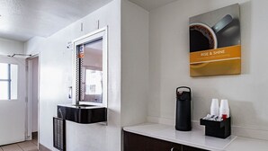Een receptiegedeelte van een hotel met een prikbord, een koffieapparaat en een poster die gratis koffie aanbiedt.