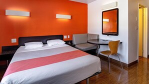 Een hotelkamer met een bed, bureau, stoel en spiegel.