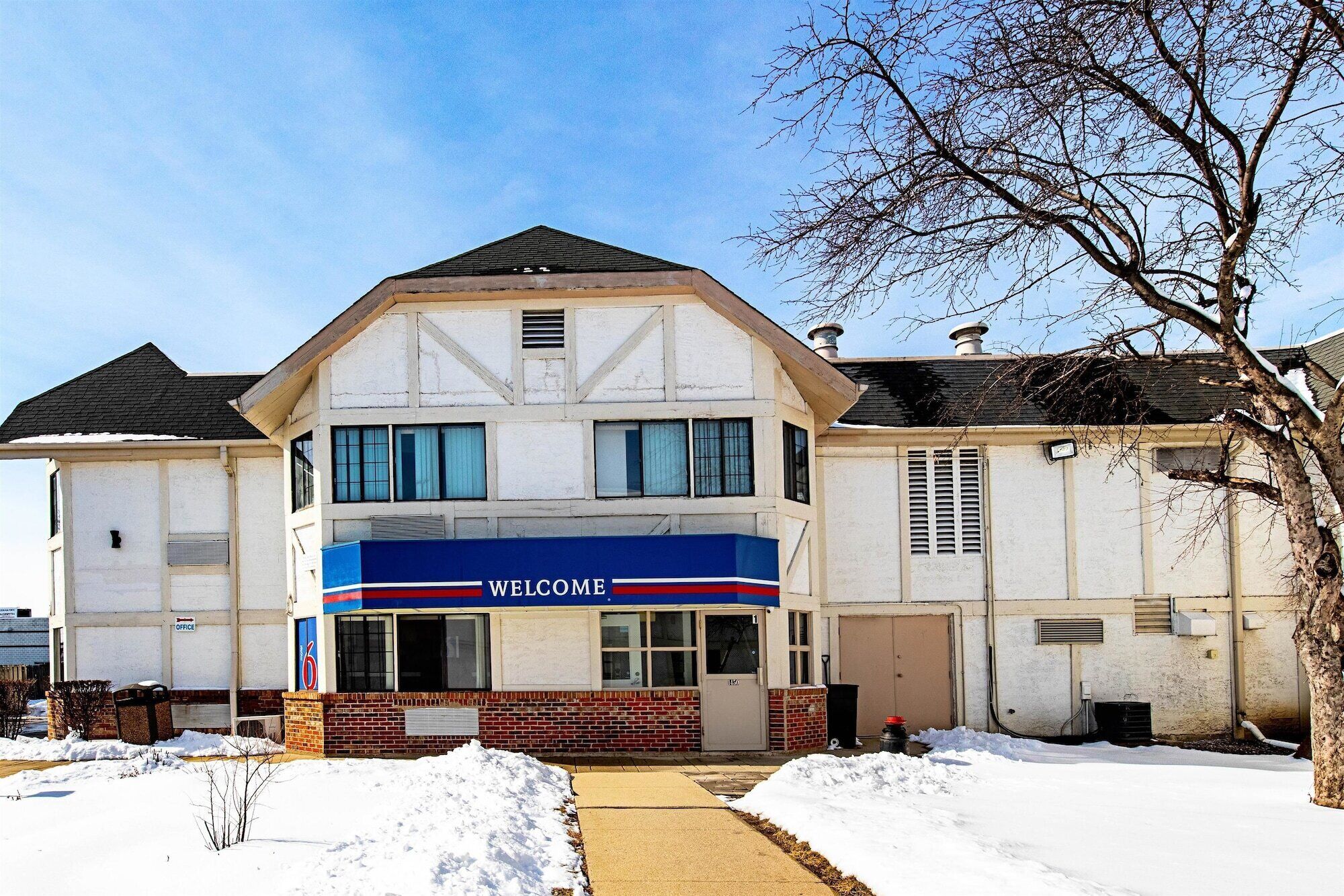 A two-story building with a 'WELCOME' sign on the front, a brick facade, and a snow-covered ground.