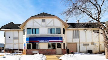 A two-story building with a 'WELCOME' sign on the front, a brick facade, and a snow-covered ground.