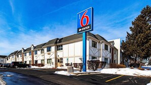 Een motel met een opvallend bord met het cijfer '6', een parkeerplaats met sneeuw en een gebouw in moderne architectuurstijl.