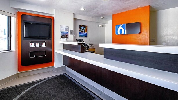 Een modern ingerichte hotelreceptie met een receptiebalie, een digitaal scherm en een beveiligingscamera.