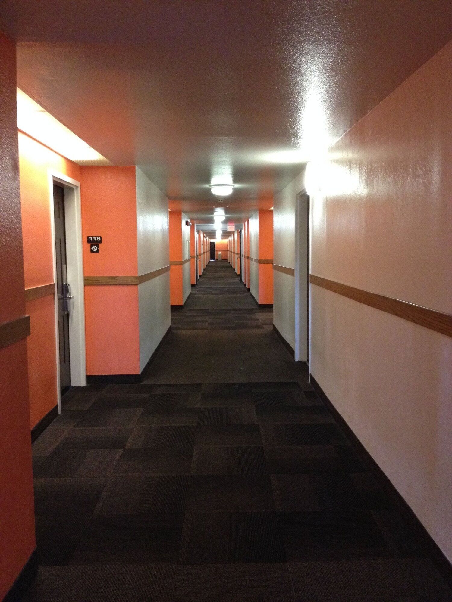 En lång, smal hall med orange väggar och ett heltäckningsmatta på golvet, som leder fram till en dörr med nummer 119.
