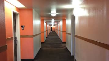 A long, narrow hallway with orange walls and a carpeted floor, leading to a door marked with the number 119.