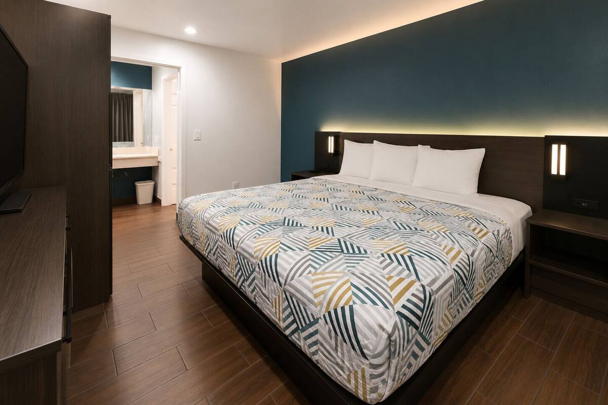 A modern hotel room with a large bed, a desk, and a bathroom visible through an open door.
