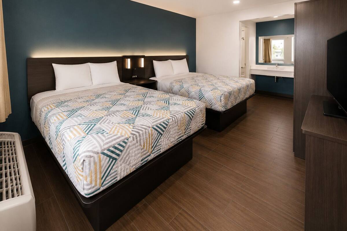A hotel room with two beds, a TV, a desk, and a bathroom visible through an open door.