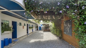A narrow alleyway with a gravel path, blue doors, and a wooden fence. - Pousada Canário Azul (Bombinhas)