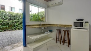 A compact kitchen with a built-in microwave, a small refrigerator, and a window overlooking greenery. - Pousada Canário Azul (Bombinhas)