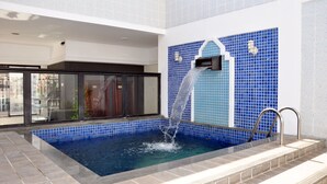A swimming pool with a water feature, tiled walls, and a glass door entrance. - Machado's Plaza Hotel (Belém)