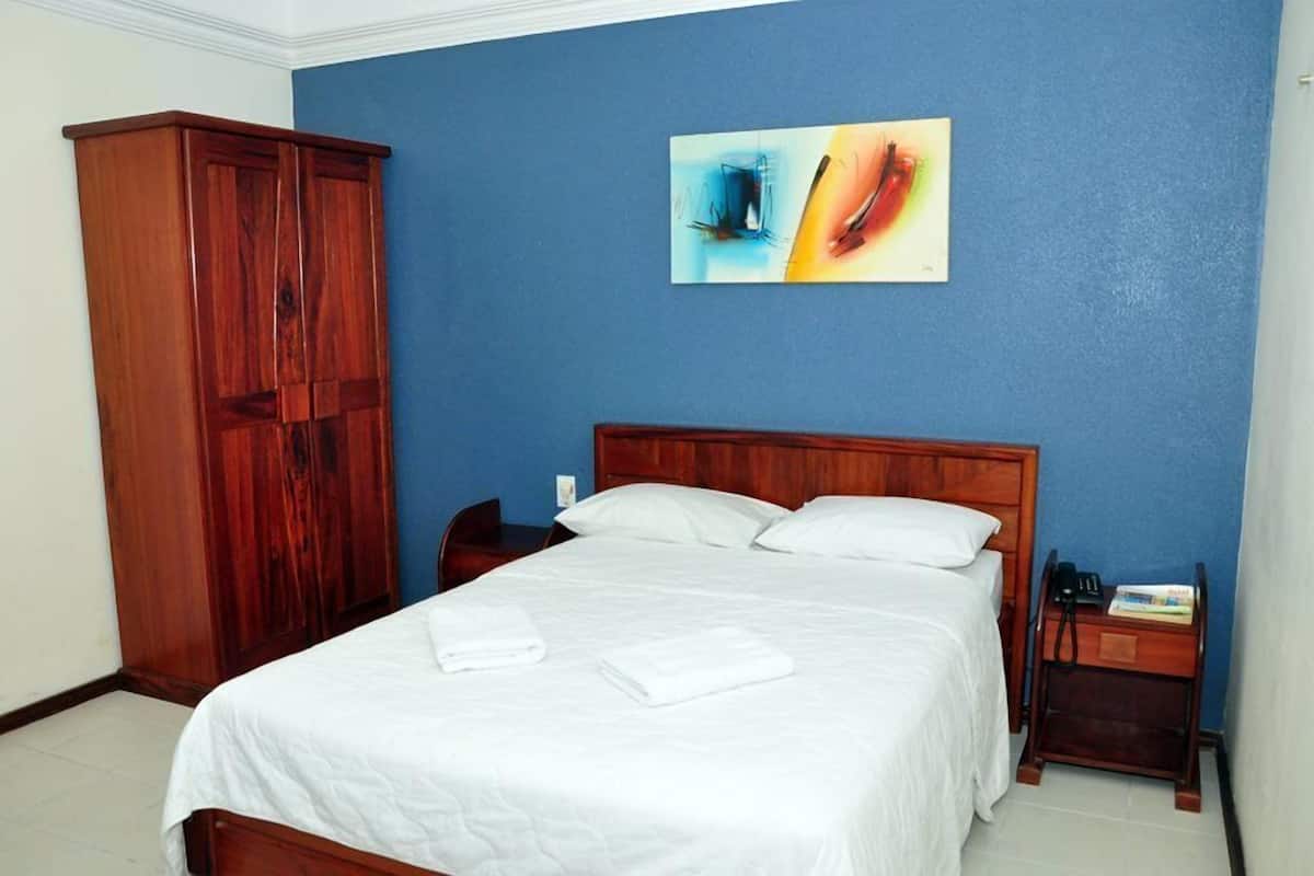 Una habitación de hotel con una cama de madera, ropa de cama blanca, una pared azul de acento y un cuadro.