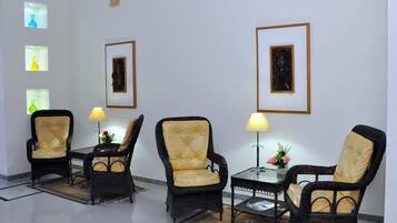 Una habitación con cuatro sillones, dos mesitas de noche con lámparas y cuadros en las paredes.