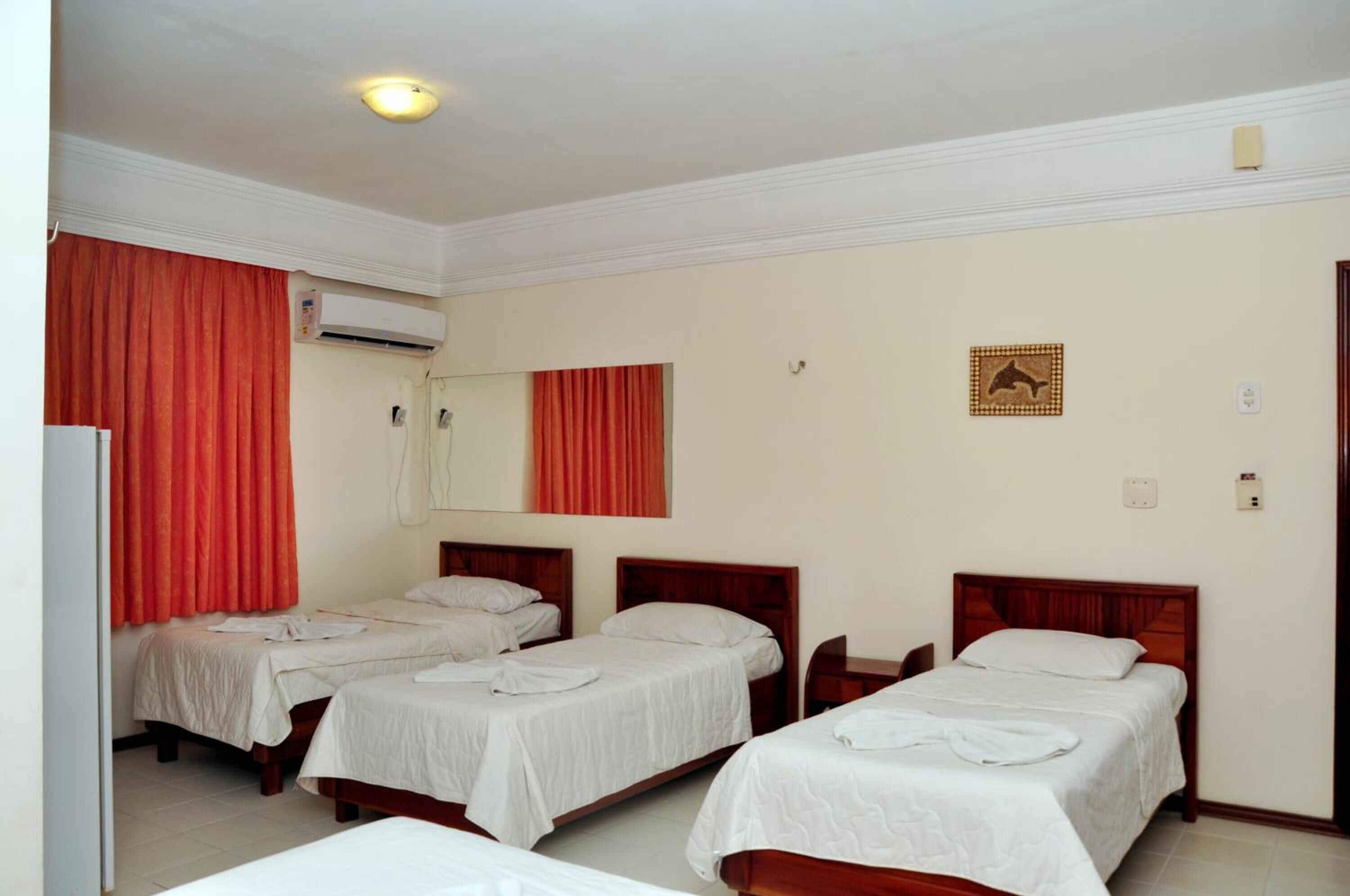 A hotel room with three single beds, a wooden headboard, a wall-mounted air conditioner, and a red curtain.