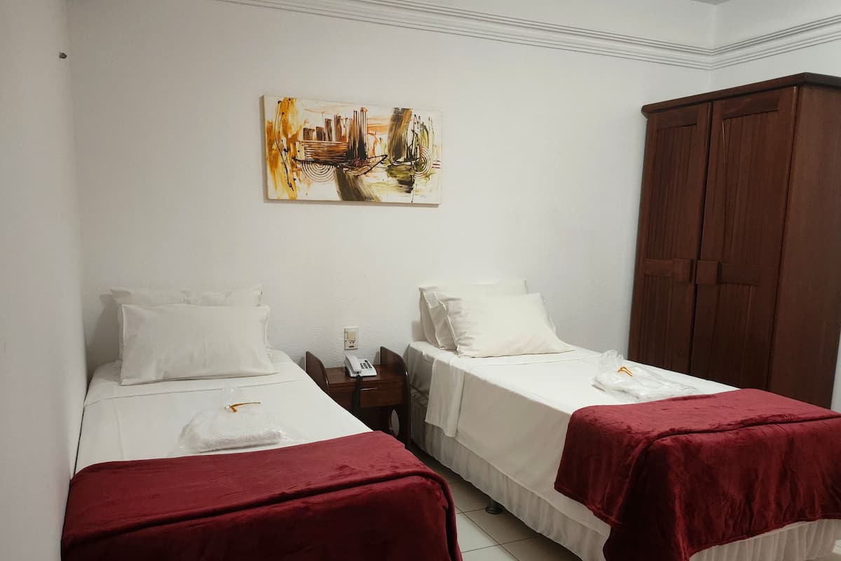Habitación de hotel con dos camas individuales, un armario de madera, un cuadro en la pared y un teléfono en la mesita de noche.
