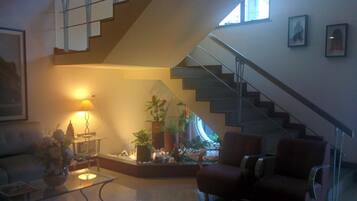 Una sala de estar con una escalera, una mesa de centro de vidrio, un sillón rojo y una lámpara.
