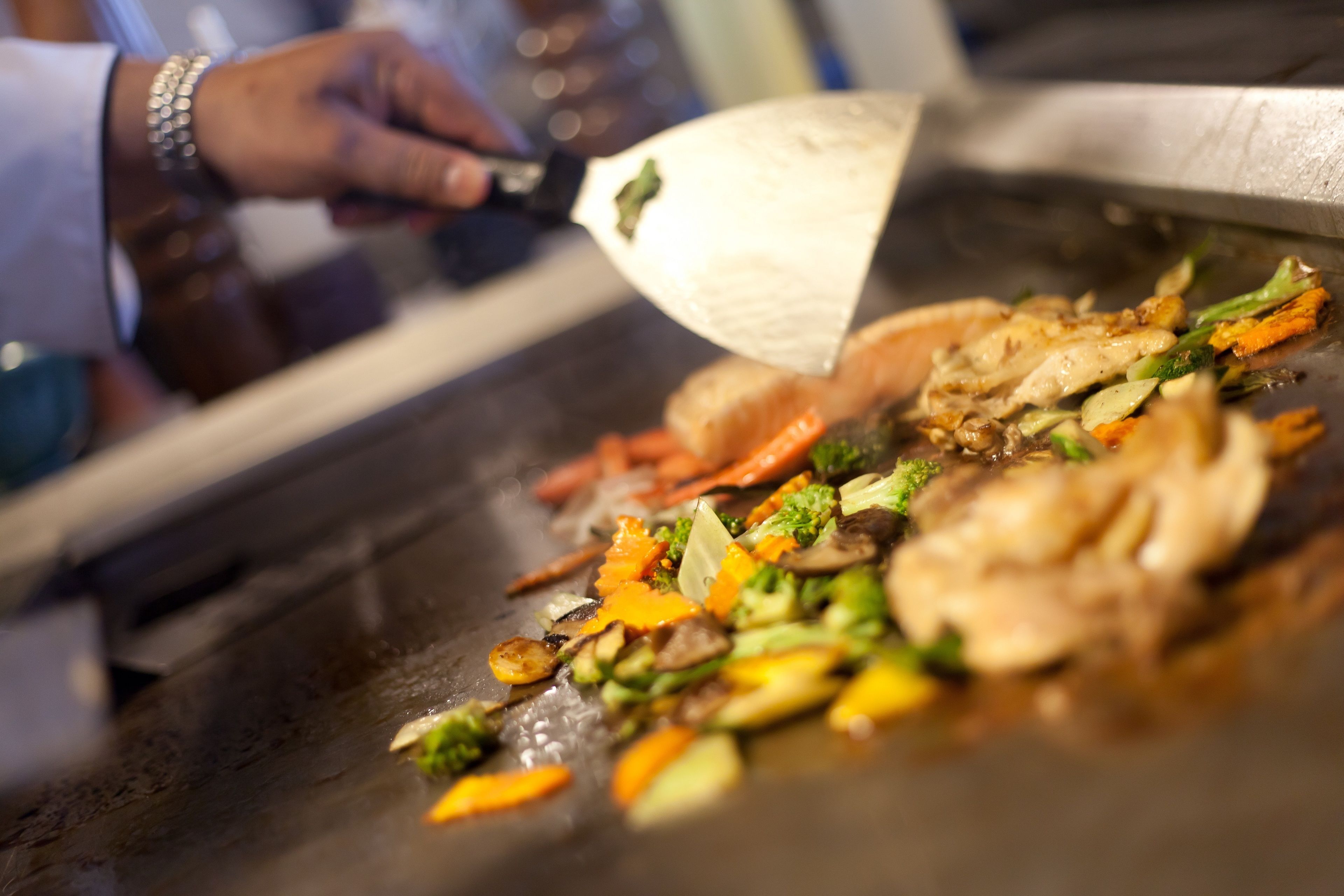 A person cooking on a large flat griddle with vegetables and meat.