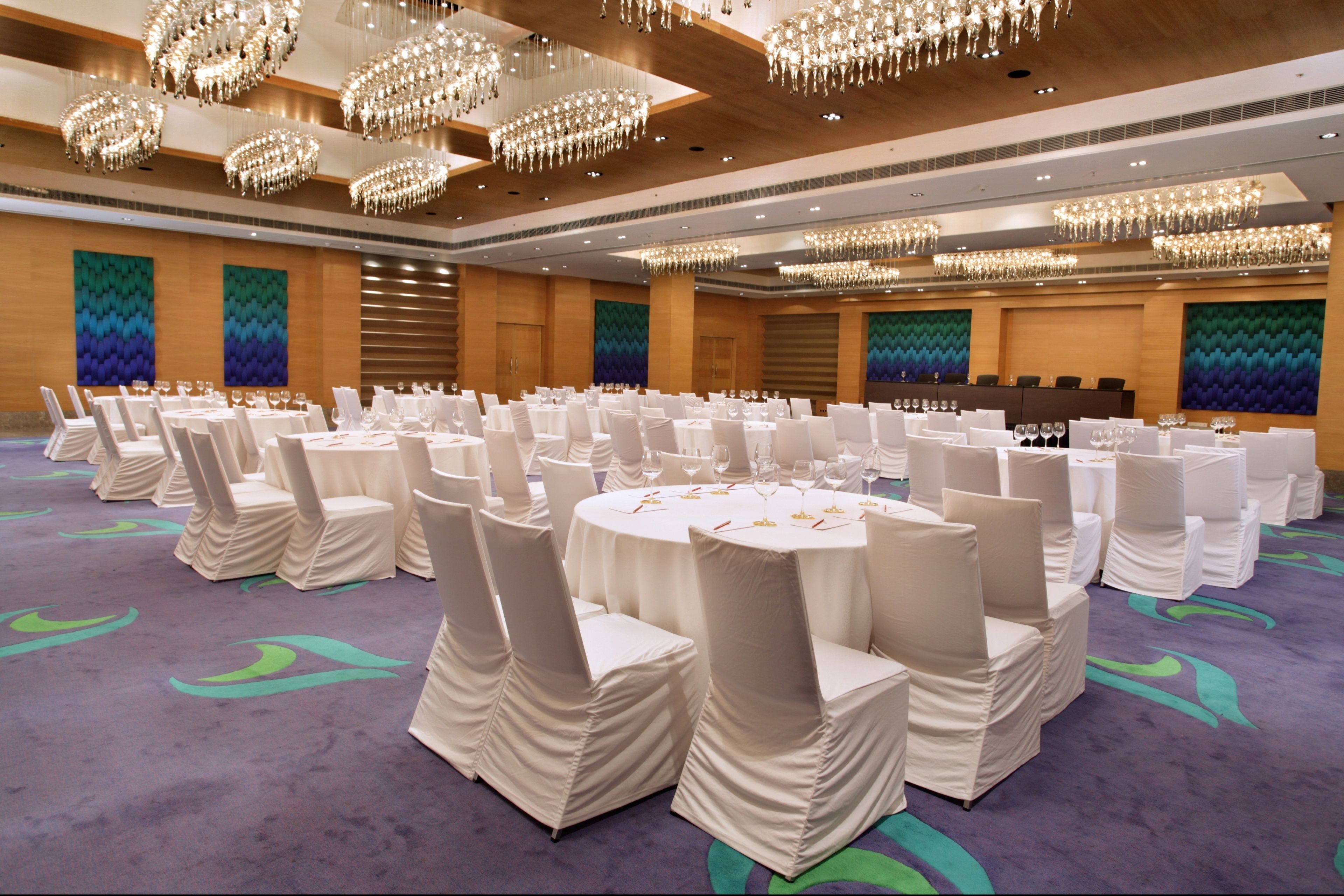 A banquet hall with round tables set for dining, surrounded by white-covered chairs.