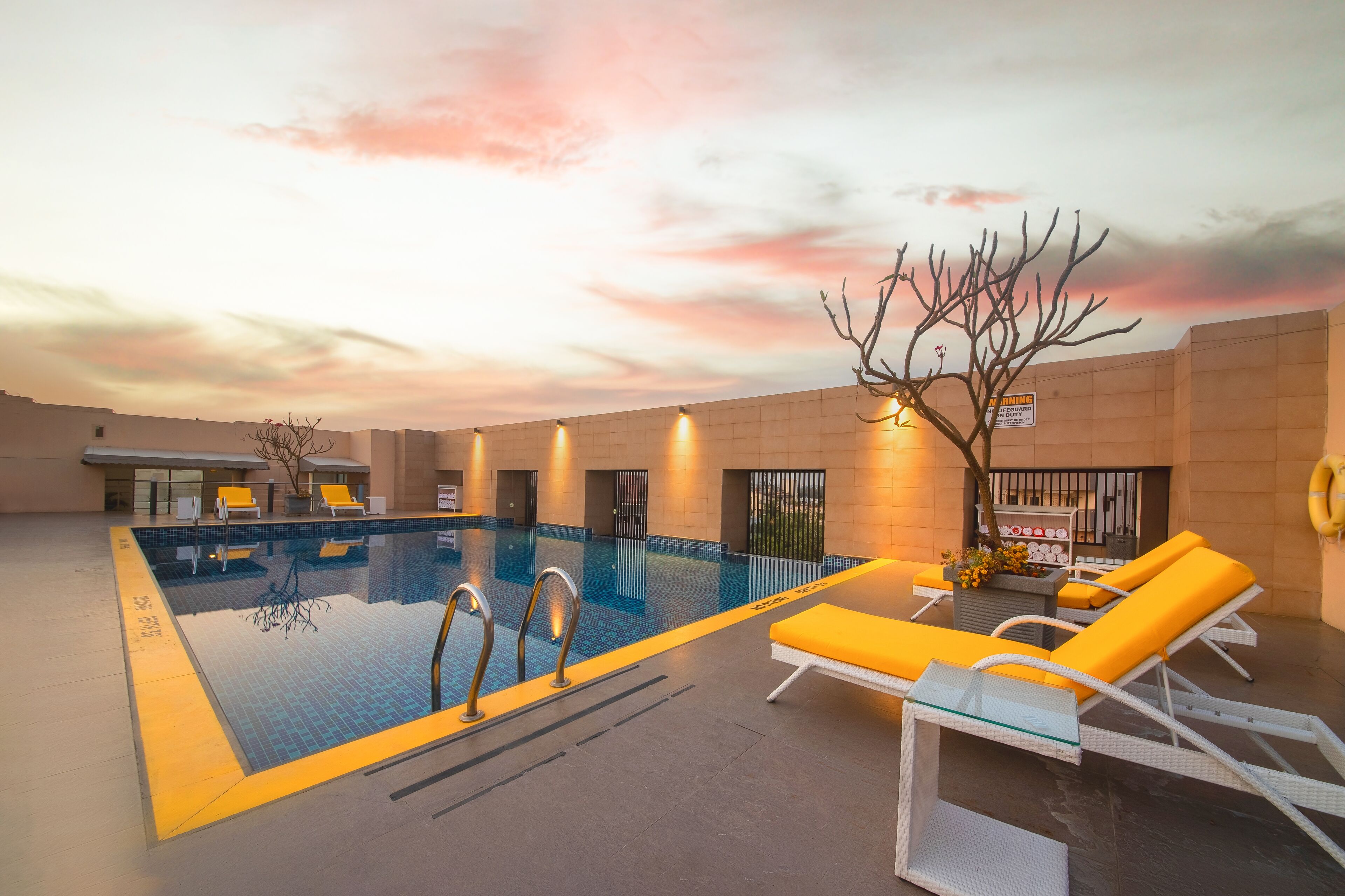 An indoor swimming pool with yellow lounge chairs and a tree.