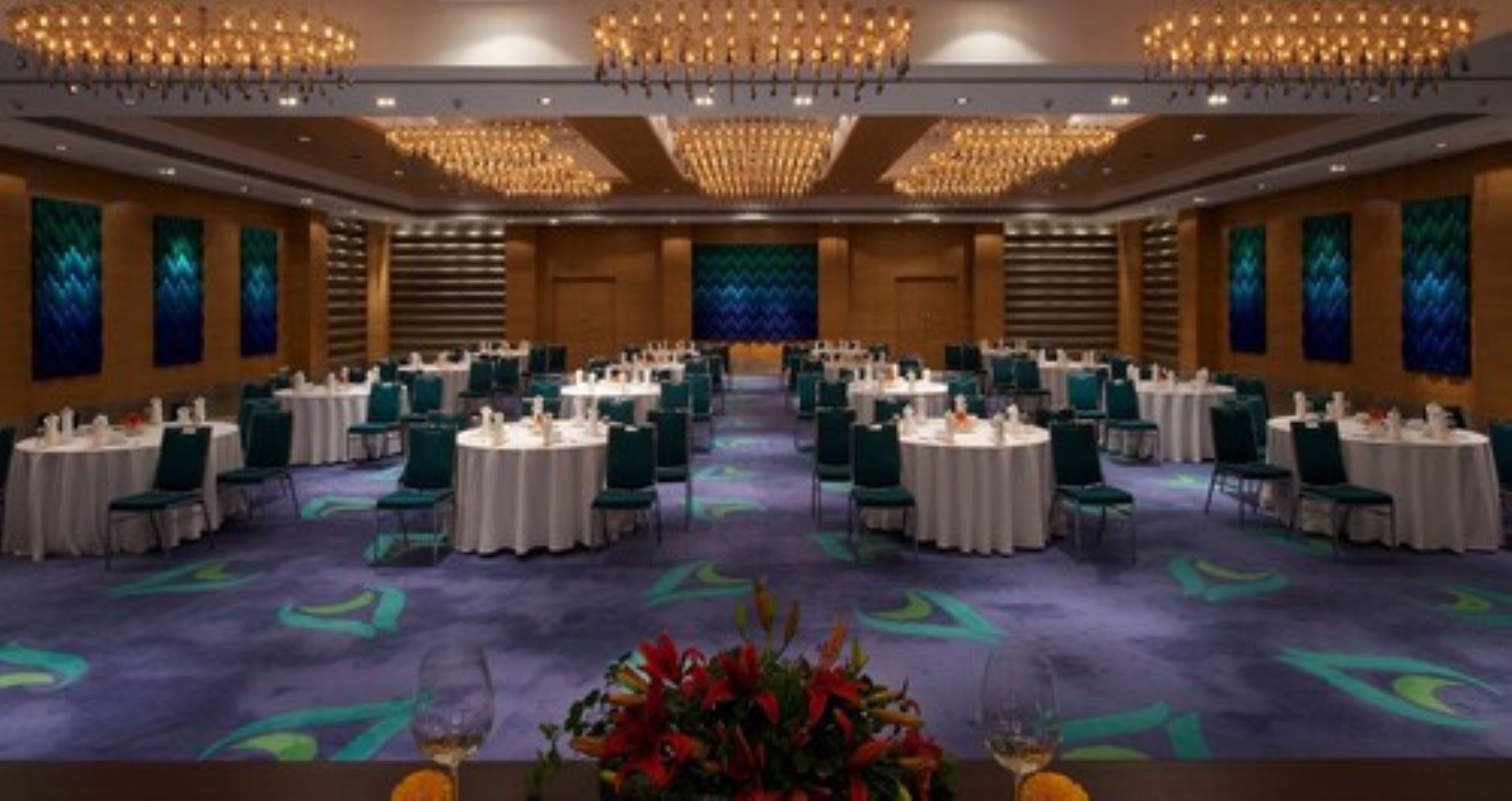 A large banquet hall with round tables, green chairs, and chandeliers.