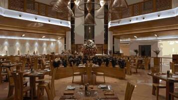 A spacious dining area with multiple tables and chairs, a central floral arrangement, and a high ceiling with decorative lighting.
