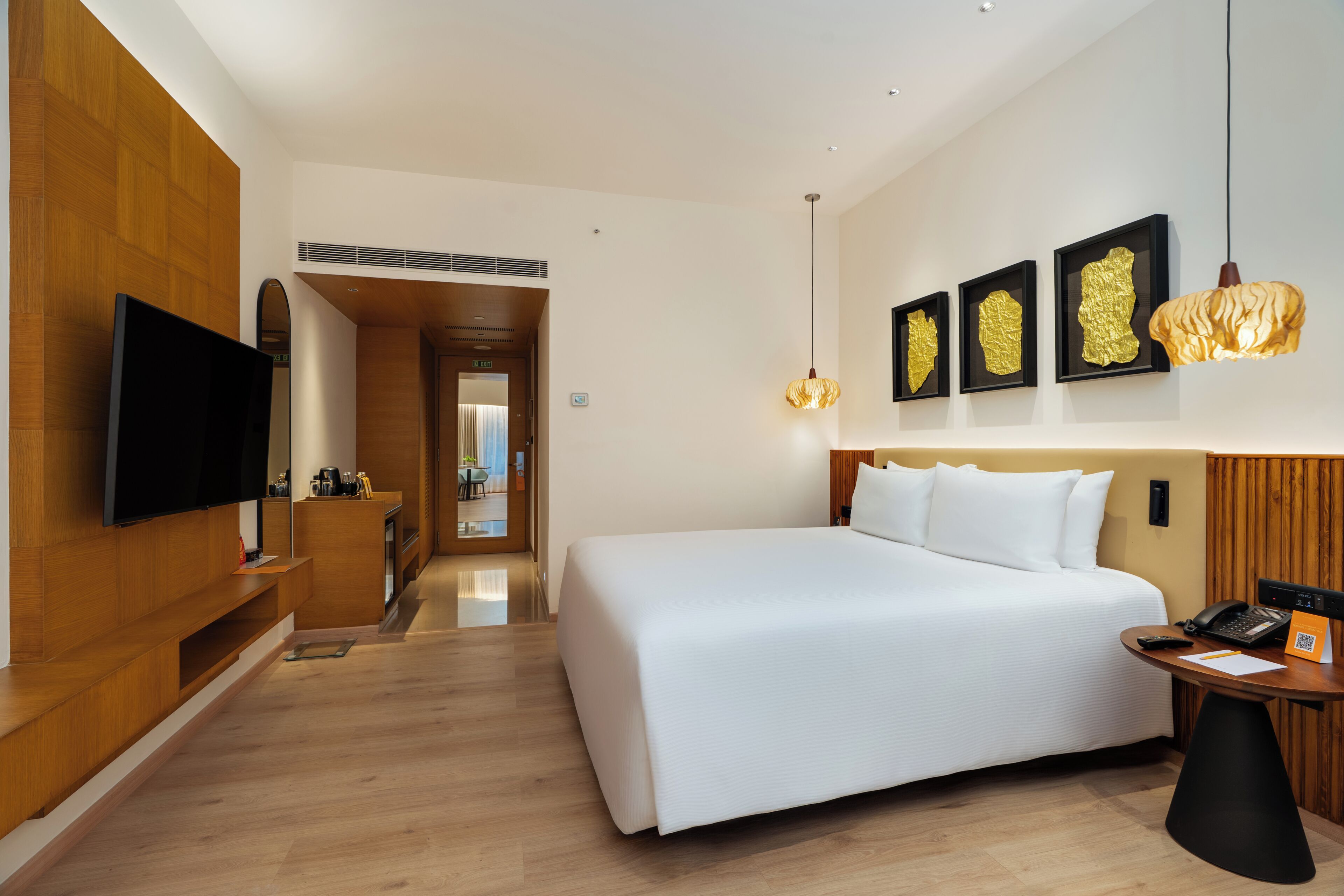 A modern hotel room with a large bed, a flat-screen TV, a desk with a phone, and artwork on the wall.