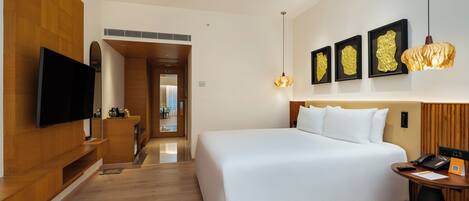 A modern hotel room with a large bed, a flat-screen TV, a desk with a phone, and artwork on the wall.
