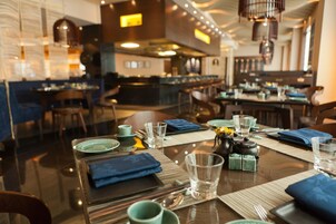 Un restaurante con mesas dispuestas para comer, con vasos de vidrio transparente y servilletas azules.