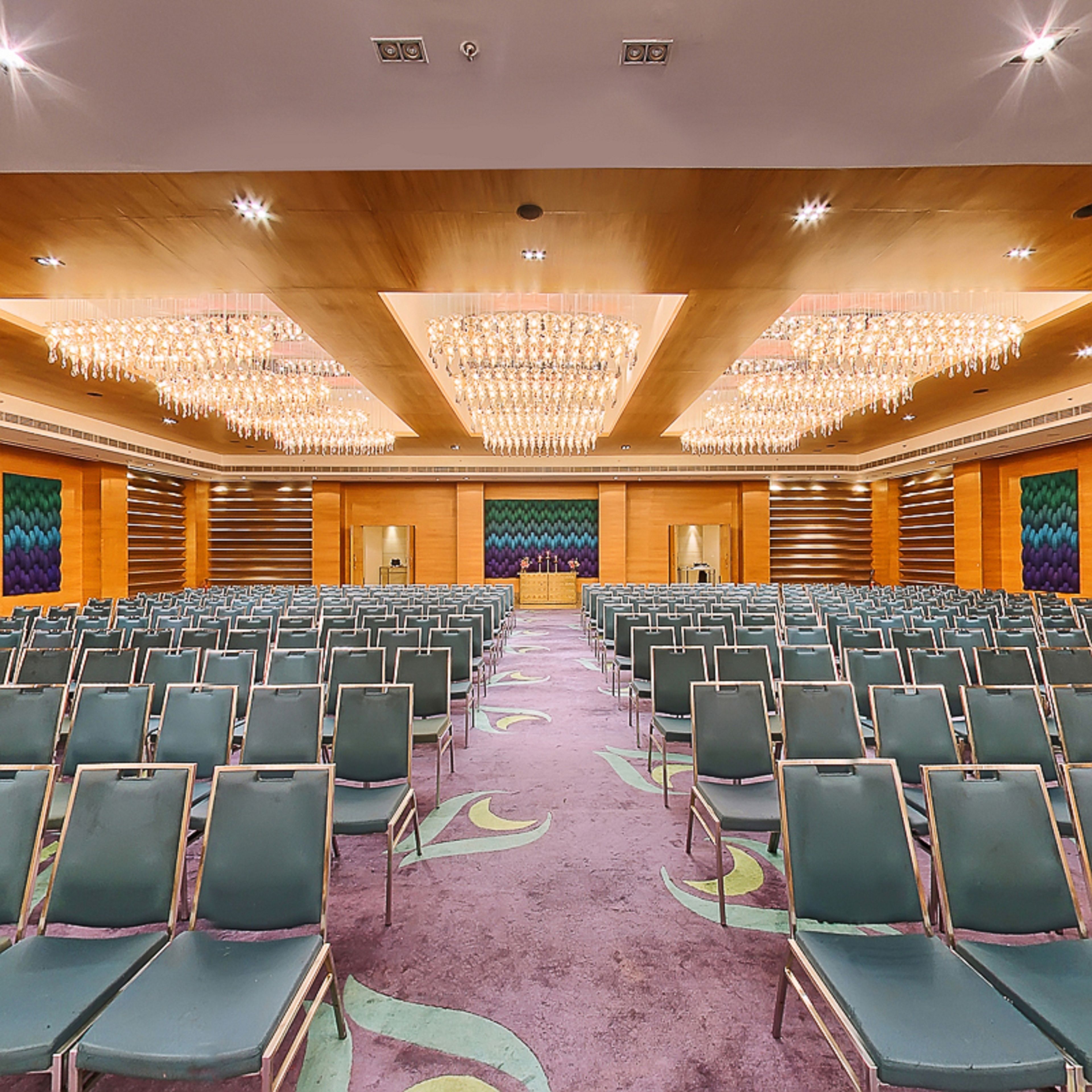 A conference room with rows of chairs, a stage, and chandeliers.