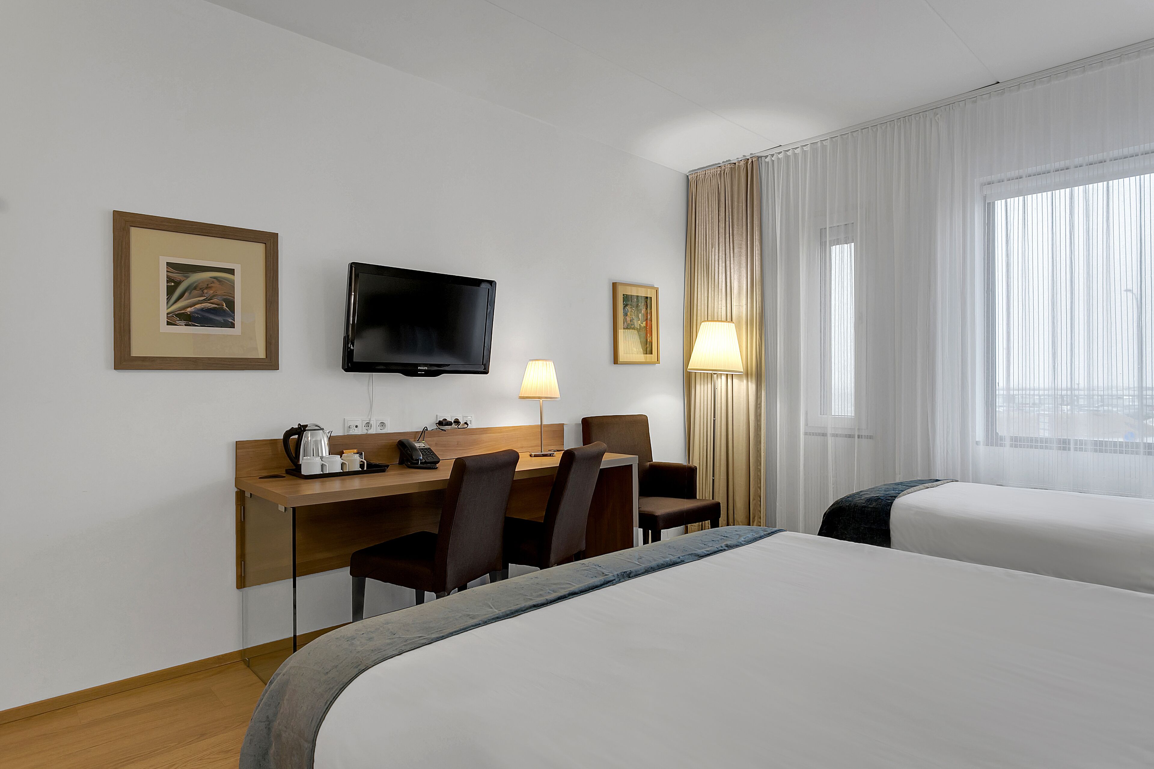 Una habitación de hotel con una cama, un escritorio con silla, un televisor y una ventana con cortinas.
