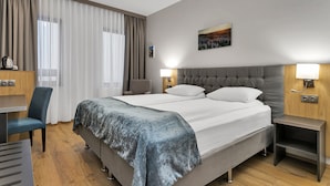 Ein modernes Hotelzimmer mit einem großen Bett, einem Schreibtisch, einem Stuhl und einem Nachttisch.