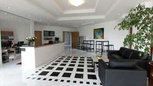 Ein modernes Wohnzimmer mit einem schwarz-weißen Fußboden, einer schwarzen Couch, einem Esstisch und einer großen Pflanze.