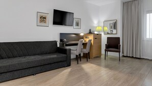 Ein modernes Wohnzimmer mit einer Couch, einem Schreibtisch mit Computer, einem Stuhl und einem an der Wand montierten Fernseher.
